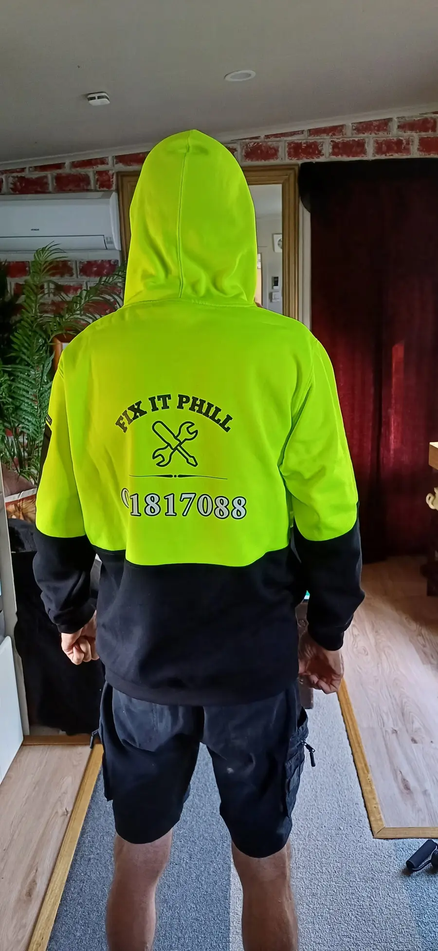 The back of Phill’s hi-vis hoodie, printed FIX IT PHILL